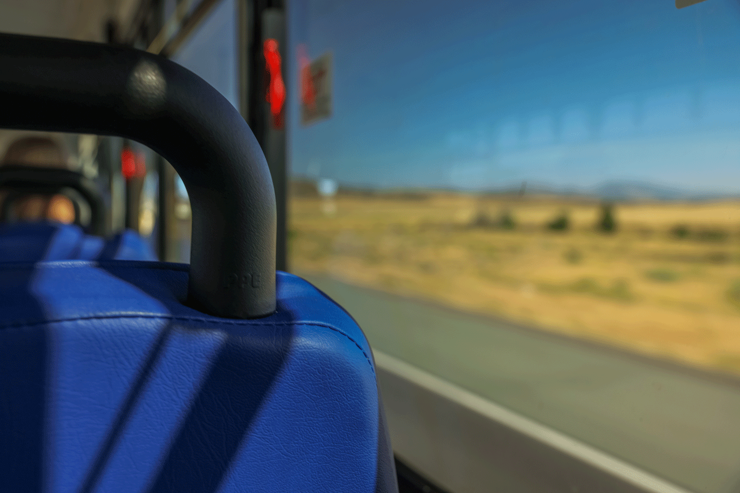 Blue bus seat in the foreground, with a blurred view of fields and sky through the bus window in the background.