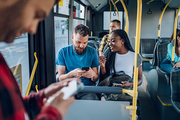 People sitting on a bus, some using their phones; a man and woman in the middle seats look at a phone together and talk, while others are focused on their devices.